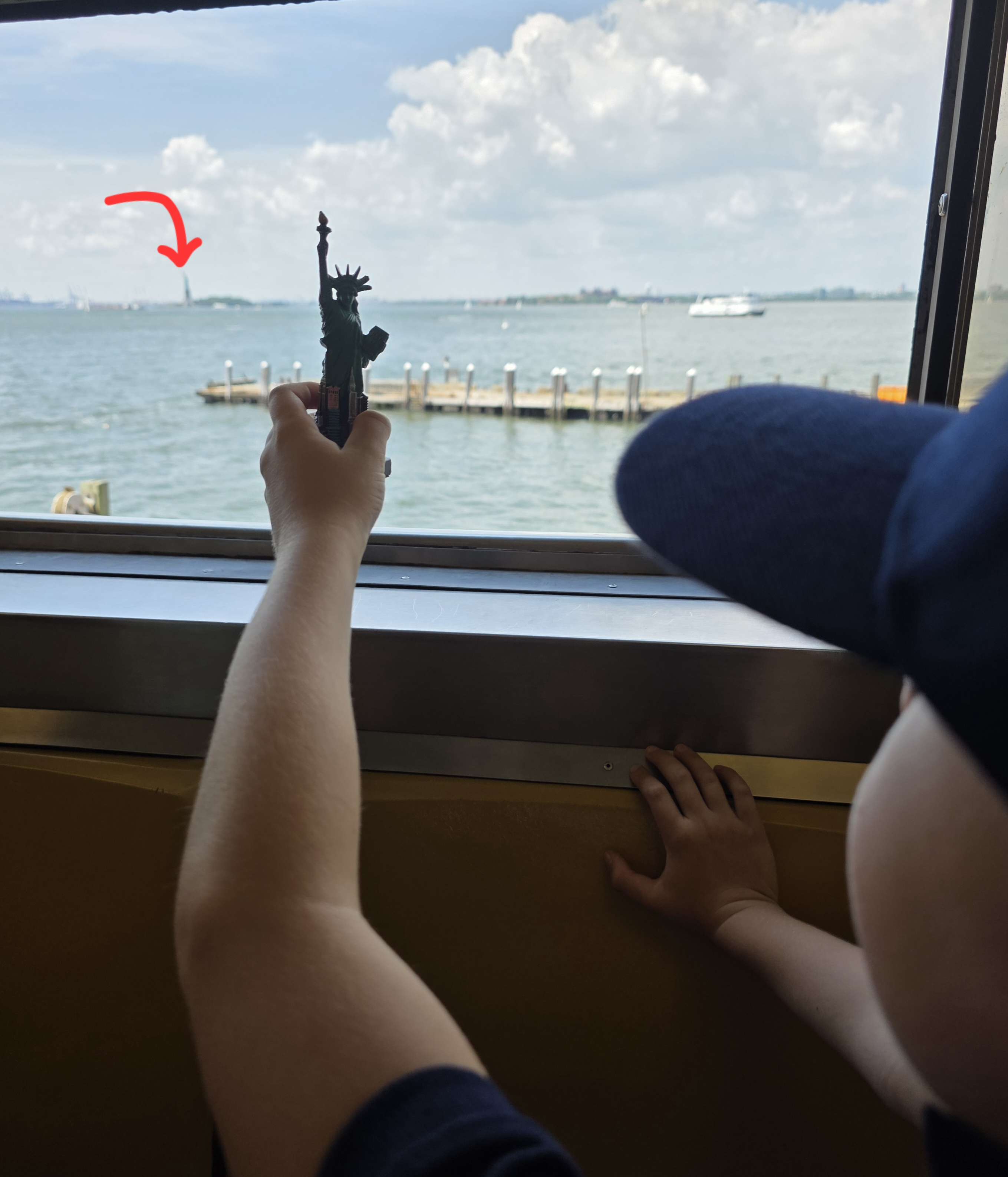 A child holding a small Statue of Liberty souvenir up to the window, with the harbour outside.