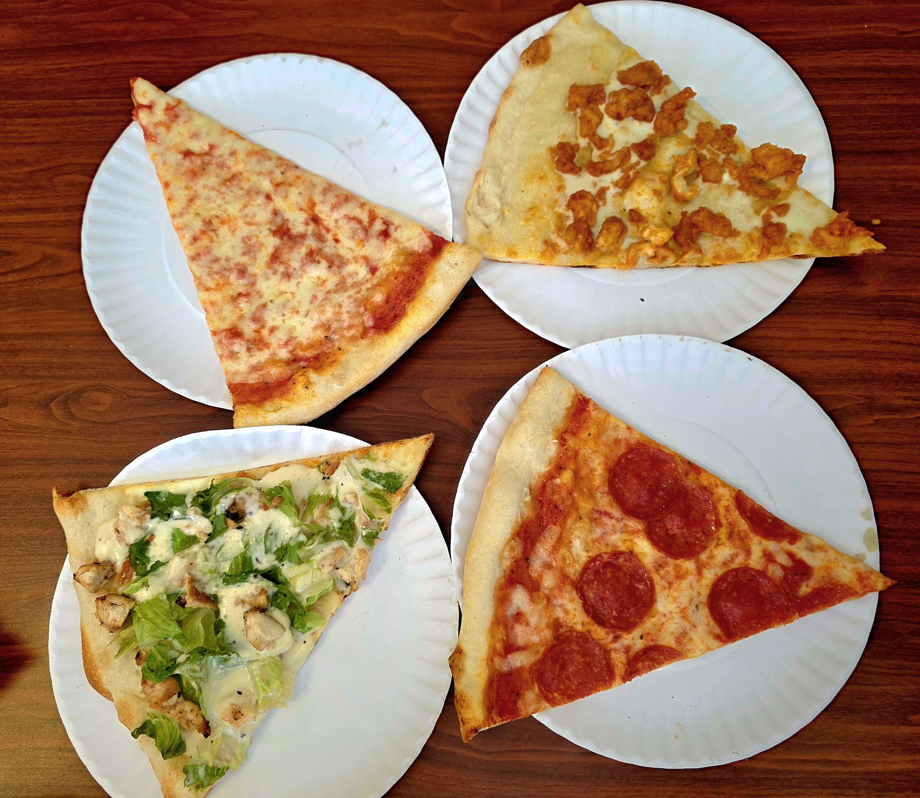 Four slices of New York pizza on paper plates.