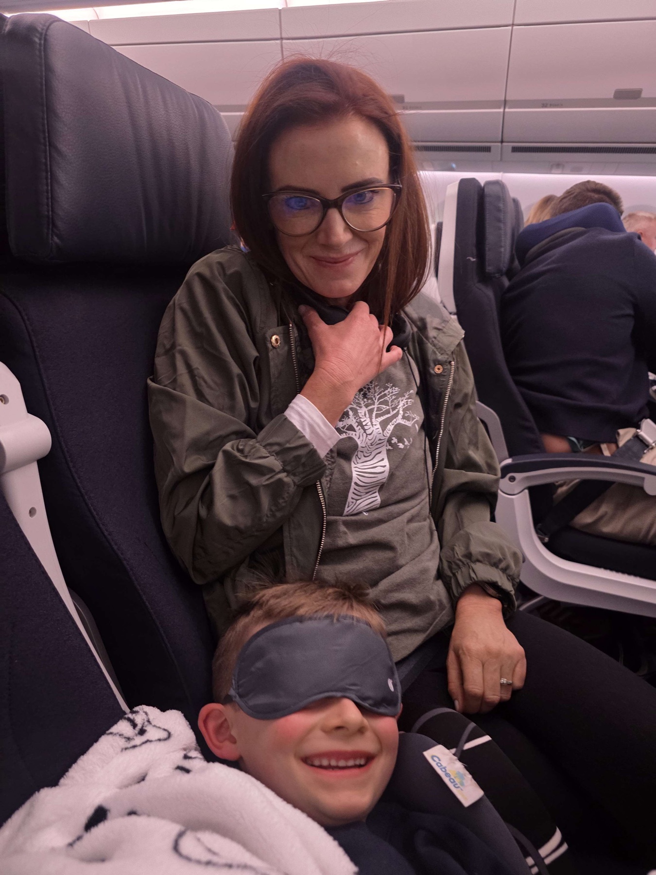 A woman and a smiling child seated together in an aeroplane cabin.